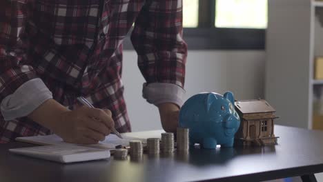 young man counting coins in a piggy bank to save money, buy a house, financial and economic concepts. monthly expenditure accounts and debt repayments using calculators and tax documents at home.