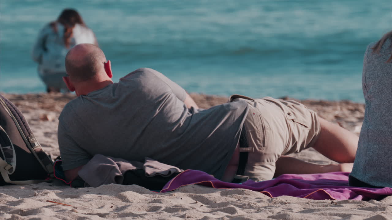 Man laying on a purple blanket at the beach, while looking at the sea