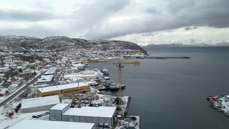 Drohne-Enthüllt-Verschneite-Winterlandschaft-Eines-Fischerdorfes-Am-Polarkreis,-Kran-Im-Hafen