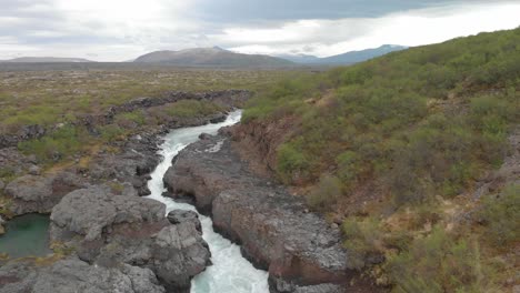 aerial view of river to the beautiful waterfall barnarfossar going through a rock formation in lush icelandic landscape with a majestic mountain in the background
