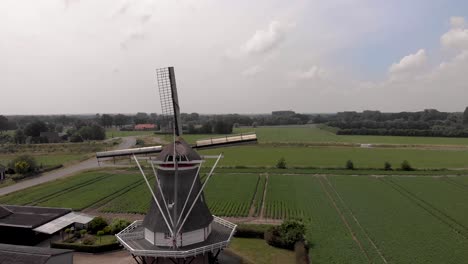 typical dutch windmill with wicks in countryside of the netherlands seen from behind closing in showing the wider flat agriculture landscape