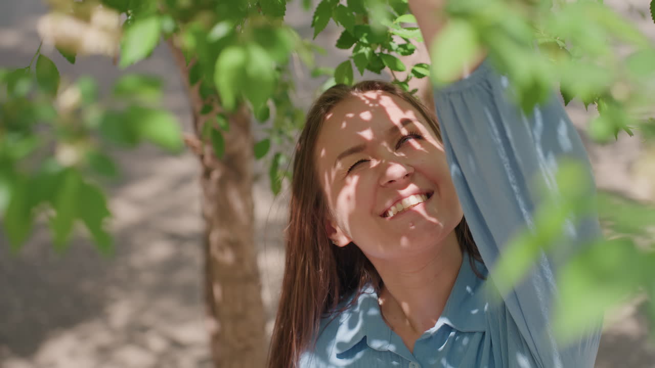 Donna che si gode il paesaggio estivo del parco, membro caucasica del team che gioca allegramente con la natura nel parco, donna con occhiali da sole che allunga la mano verso un ramo fiorito nella rilassante cornice del parco