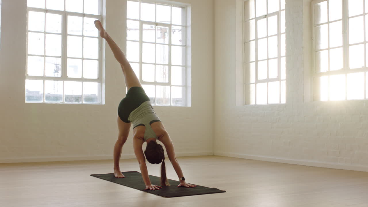 mujer de yoga saludable practicando pose de perro boca abajo de tres patas disfrutando de un estilo de vida físico haciendo ejercicio en un estudio de entrenamiento que estira el entrenamiento en una colchoneta de ejercicios al amanecer