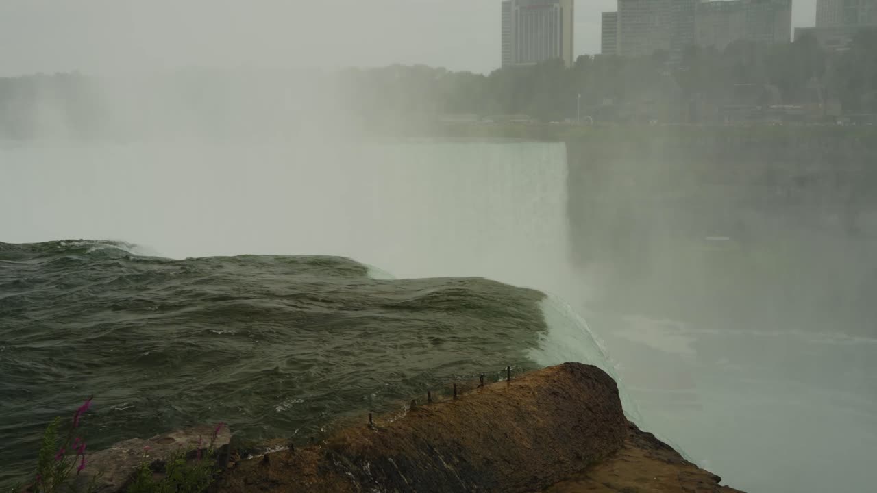Mist rises from the roaring drop of Niagara Falls as rushing water surges over the rocky ledge into the gorge below