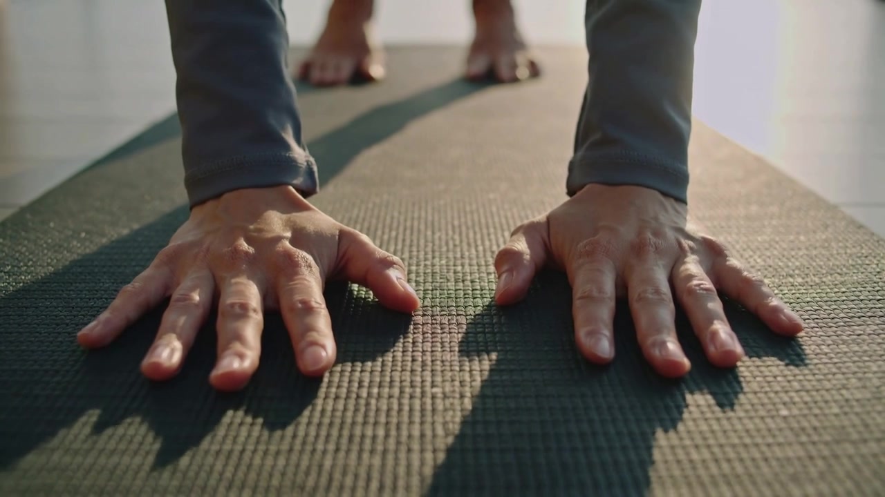 Posizionando le mani, una persona con maglia a maniche lunghe preme i palmi sul tappetino da yoga in studio, stabilizzando la posizione del plank.