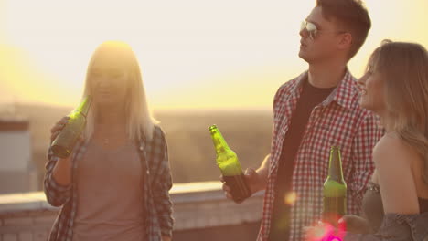 three girls and three boys enjoying time on the roof. they smile and communicate with each other. they drink beer from green bottels and have fun in the plaid shirts.