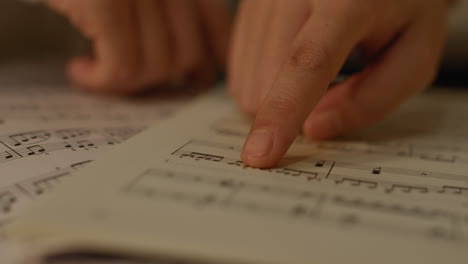 close up on girls fingers following over notation in the music score book