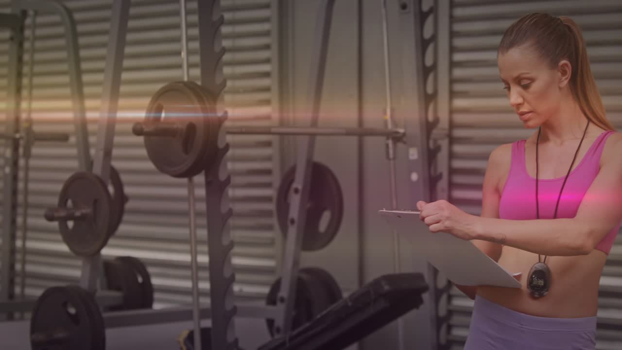 Fitness coach checking clipboard and starting stopwatch, coaching reps, gesturing near squat rack