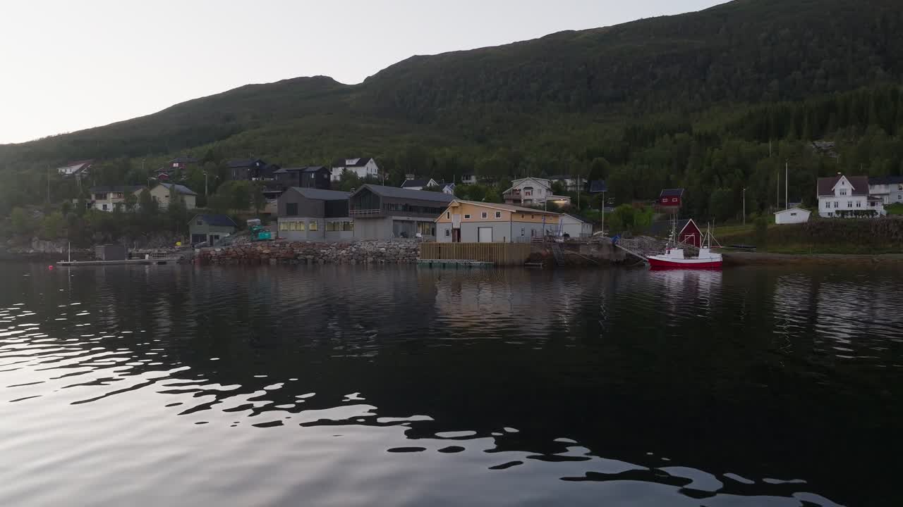 Drone flying low over water on coast of rural Norwegian town with green hills and nature
