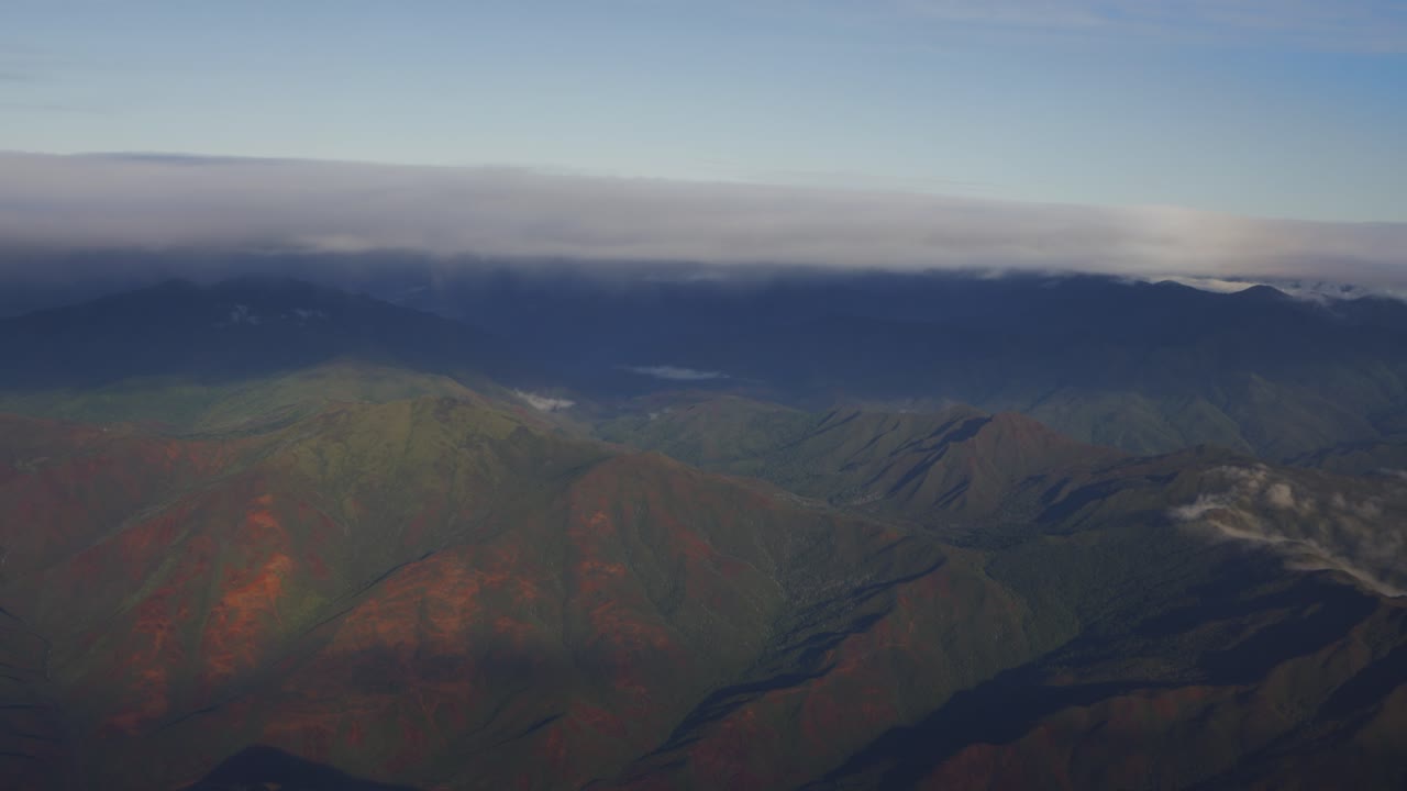 una hermosa escena de nubes y una cordillera boscosa vista desde la ventana de un avión a la luz del día