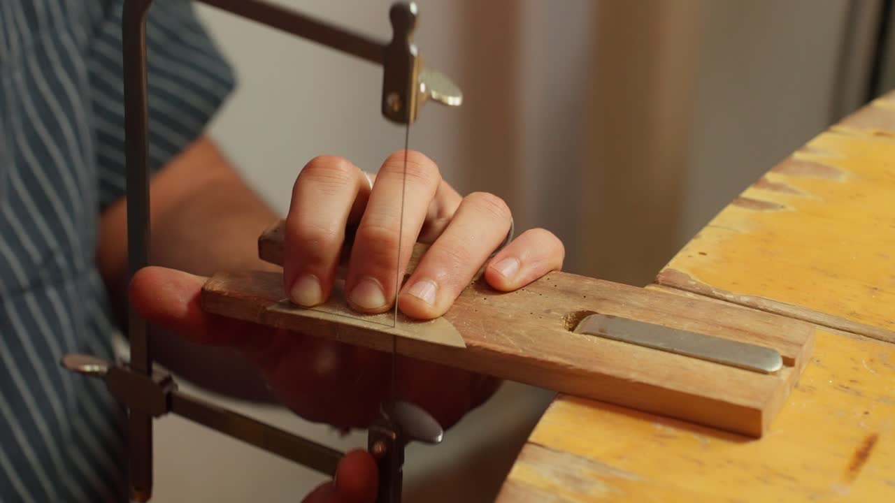 An artisan carefully saws wood to create detailed shapes, the setting is a well-lit workshop filled with tools.