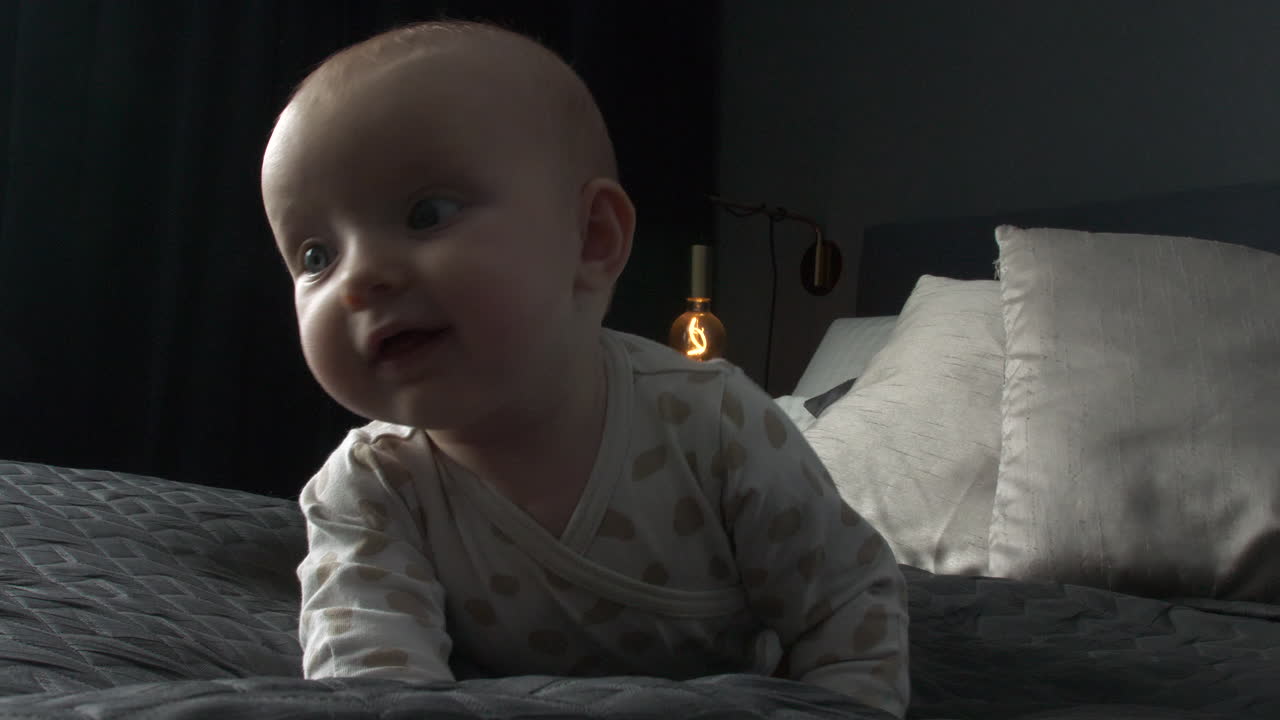 호기심 많은 눈을 가진 귀여운 여자아이가 어두운 침실에 있는 킹 사이즈 침대에 누워 있고, 가까운 추적 샷