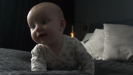 una linda niña con ojos curiosos se voltea en una cama tamaño king en un dormitorio oscuro, toma de seguimiento cercana