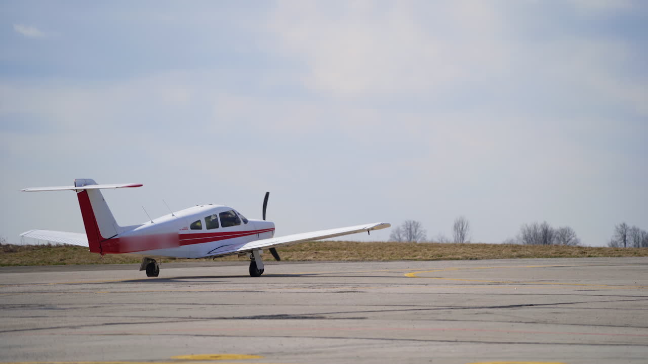 Little white airplane with red lines rides buy the empty aerodrome. Aircraft is taking off.