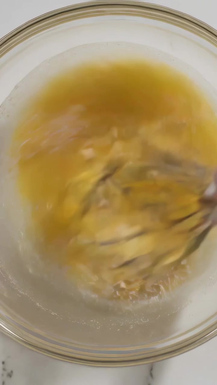 Video verticale: Inizio della frusta, mano che sbatte le uova in una ciotola di vetro sul bancone della cucina, frusta d'acciaio.