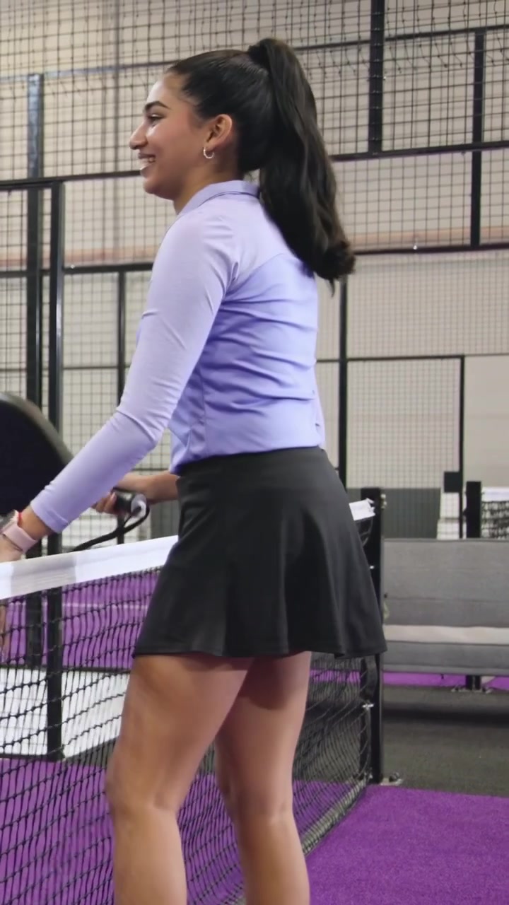 Vertical video: Entering right, lilac-top woman walking on court warming up with paddle, copy space