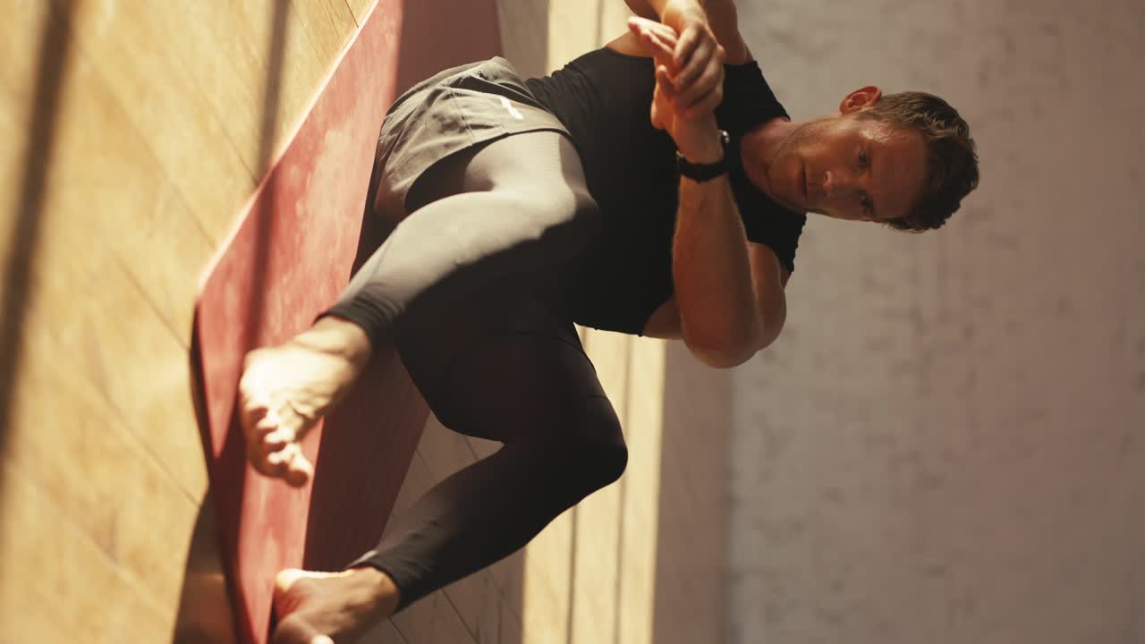 Vertical video of a man in a black sports summer uniform doing exercises for pumping the abdominal muscles on a special Red mat in the Sunny Hall