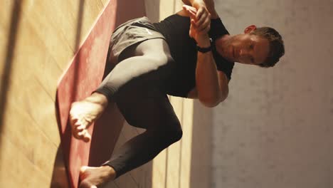 vertical video of a man in a black sports summer uniform doing exercises for pumping the abdominal muscles on a special red mat in the sunny hall