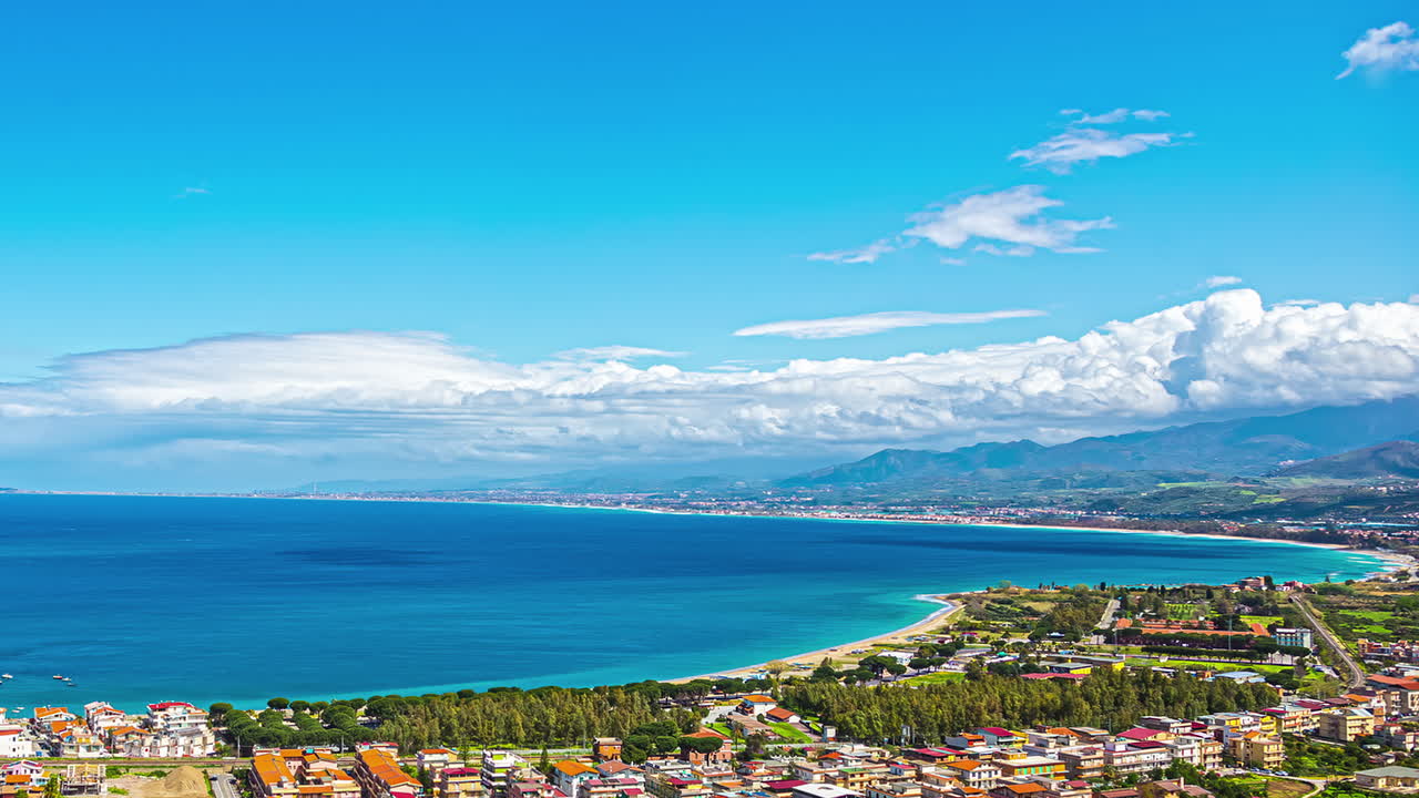 시칠리아에서 화창한 날 동안 해안선, 모래사장, 해안 마을이 있는 활기찬 푸른 바다의 드론 시간 경과