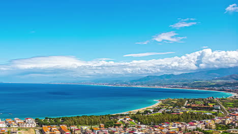 drone time lapse of vibrant blue colored sea with coastline, sandy beach and coastal town during sunny day on sicily