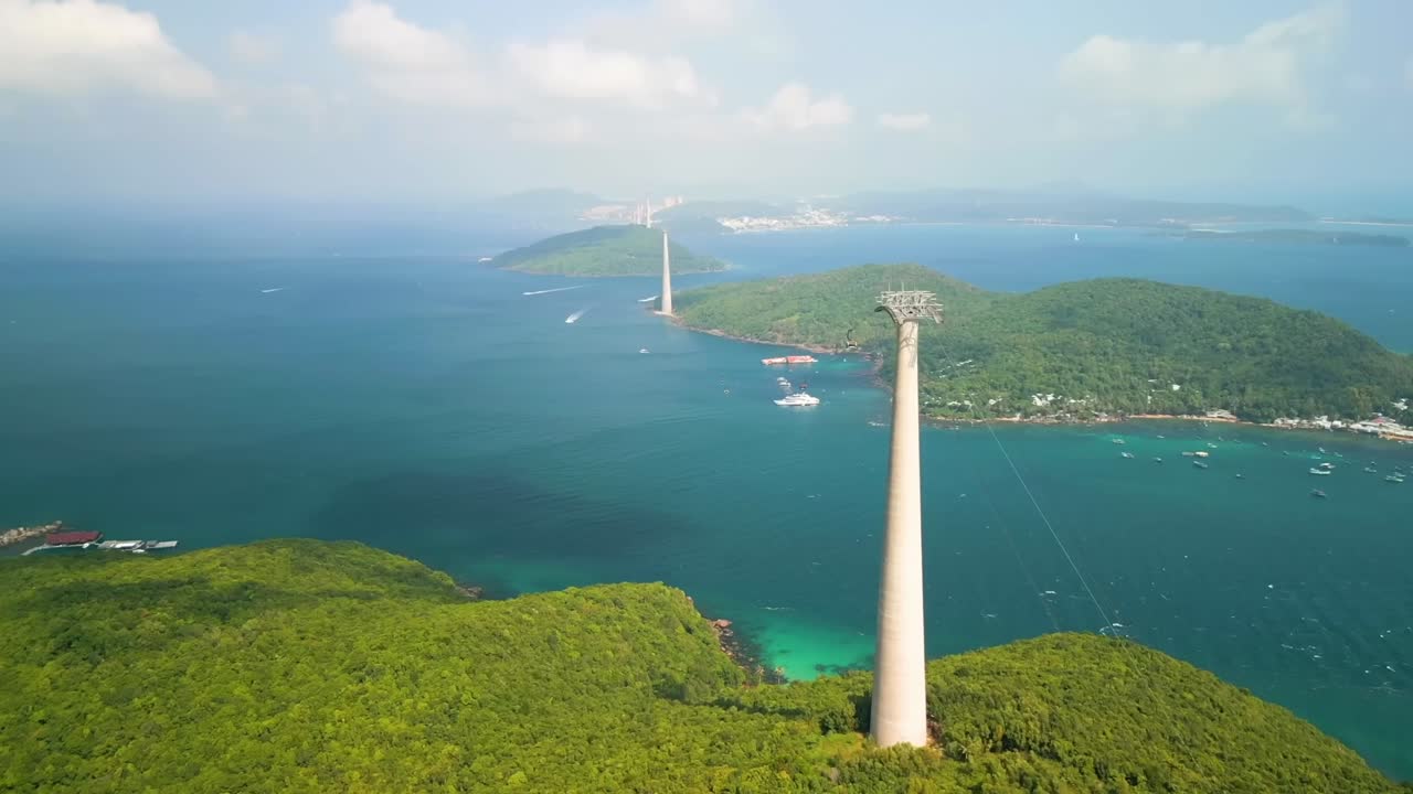 A scenic aerial view of Halong Bay showcases towering cable car pillars connecting lush islands across turquoise waters, blending engineering marvels with breathtaking natural beauty.