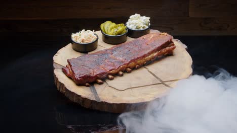 Rack-of-bbq-ribs-with-sides-of-salads-and-pickles-covered-by-a-white-smoke-medium-shot