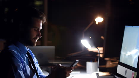 Businessman using smartphone and computer at night