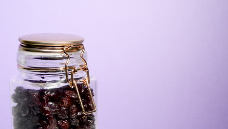 close up of an airtight mason jar rotating with dehydrated cranberry on a neon lilac background