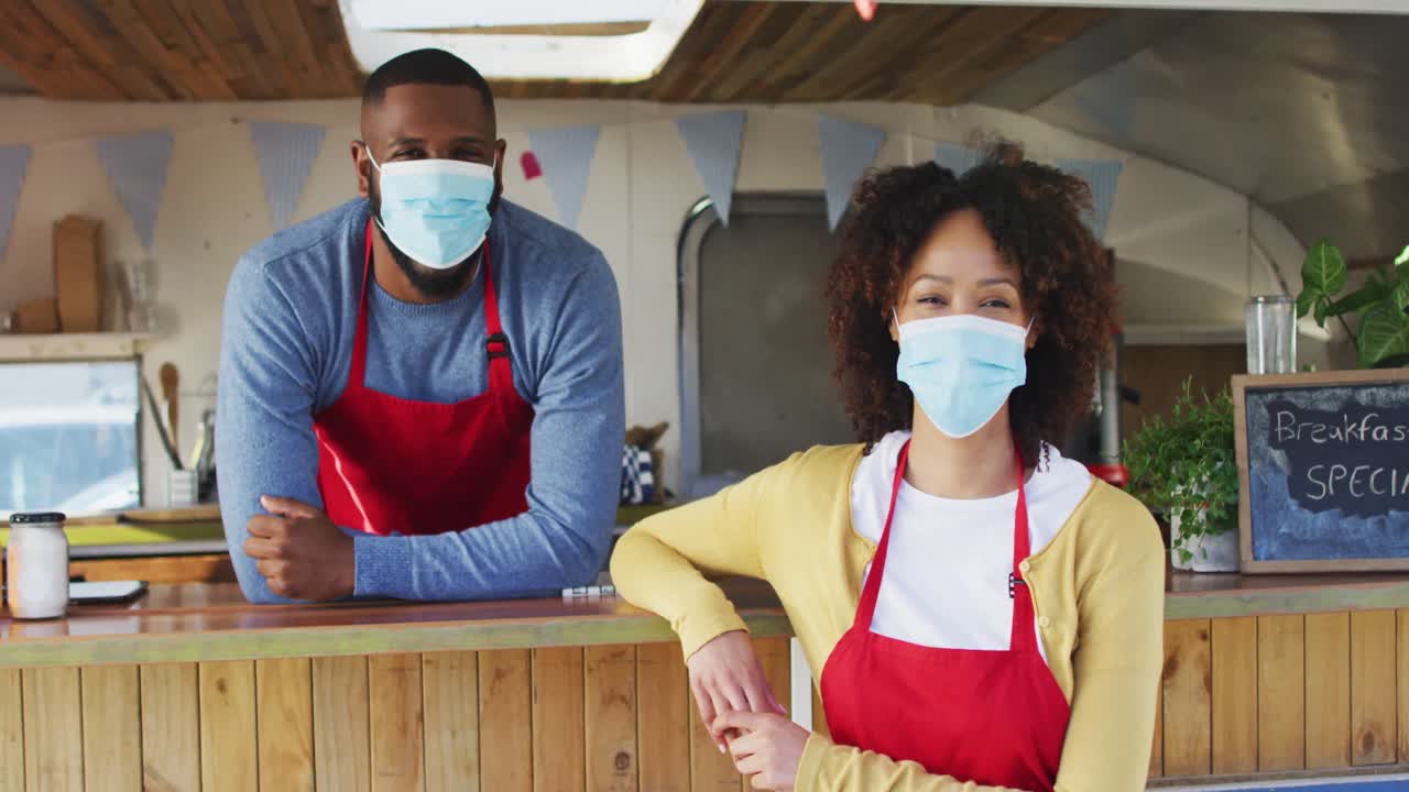 retrato de una pareja afroamericana con máscaras faciales de pie cerca del camión de alimentos