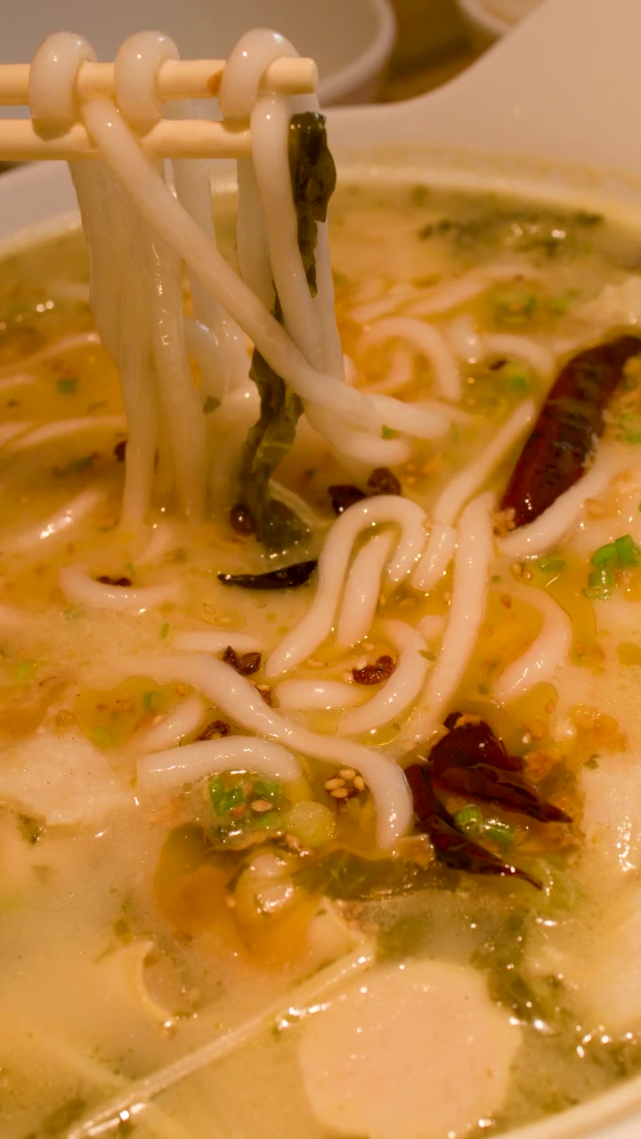 Persona che usa le bacchette per mangiare zuppa di noodle asiatica