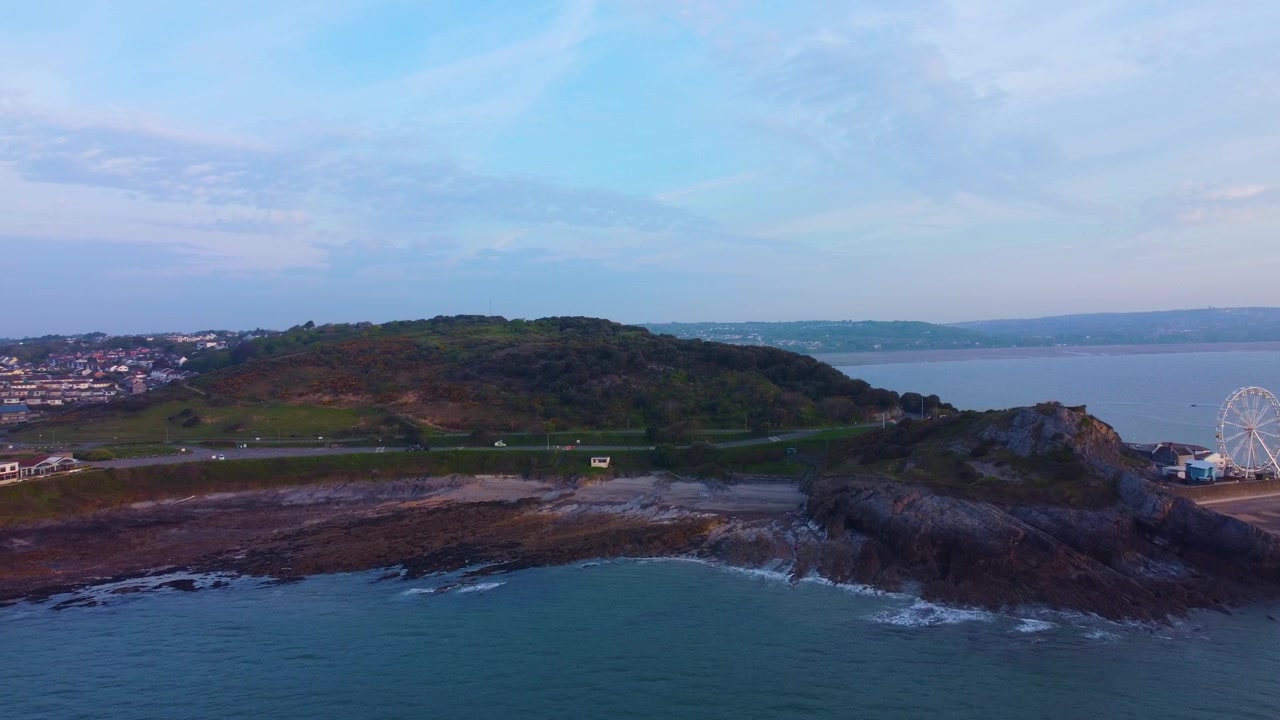 Vista aérea da Baía de Bracelet em Mumbles com colina e bela praia com imóveis de luxo ao fundo. Clipe de drone do nascer do sol na hora dourada. 4K.