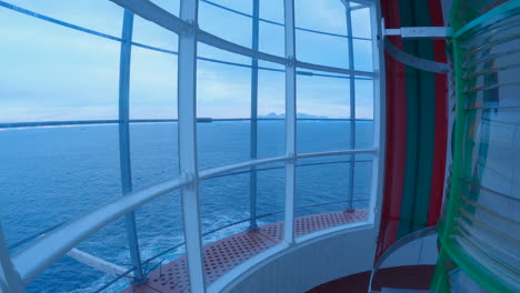 Inside-a-historic-Norwegian-lighthouse-panning-from-the-lens-to-the-ocean,-in-arctic-with-mountains-in-the-distance,-panning-right-to-left