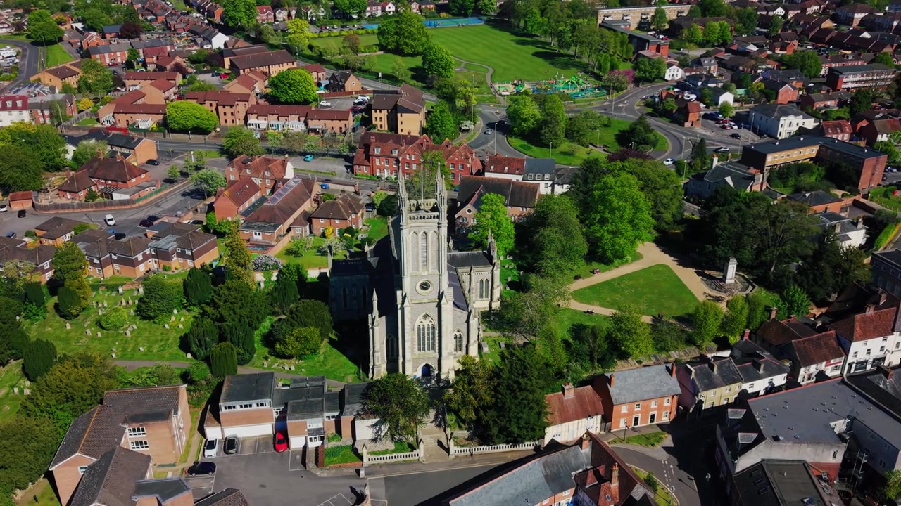 Riprese aeree con drone ad alta quota della Chiesa di Santa Maria ad Andover, che mostrano la storica torre della chiesa, il sagrato, i tetti circostanti, le strade, gli spazi verdi e il più ampio paesaggio urbano dell'Hampshire in una giornata di sole