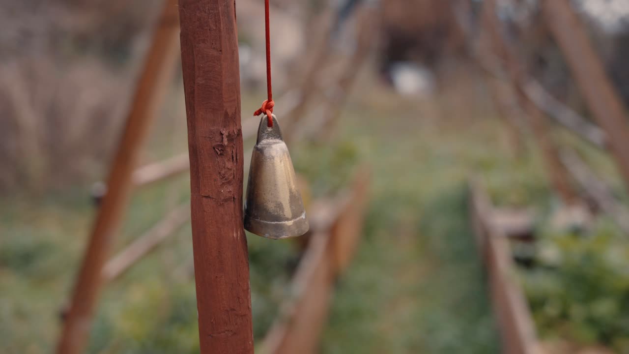 A garden bell hangs gently, symbolizing tranquility and peace. The soft green and brown hues of the garden create a serene atmosphere, emphasizing the calming presence of the bell.