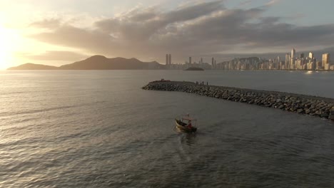 Boat-Sailing-In-The-Sea-Near-The-Molhe-da-Barra-Norte-At-Sunset-In-Santa-Catarina,-Brazil