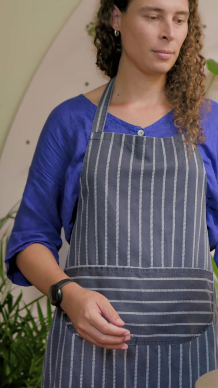 Vídeo vertical: Estendendo a mão para vaso verde, funcionários arrumando plantas para exposição na loja, avental listrado