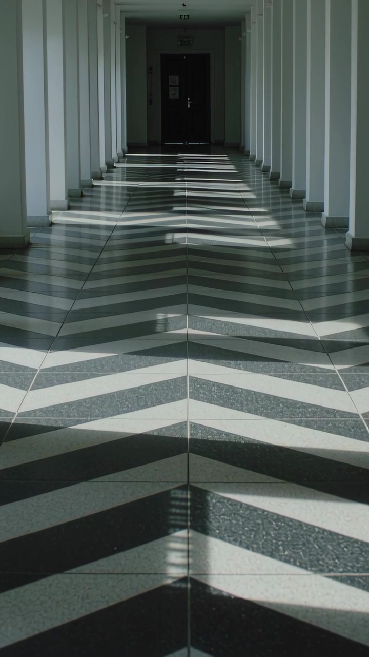 Vertical video: Streaming sunlight casting bands across chevron floor in long corridor