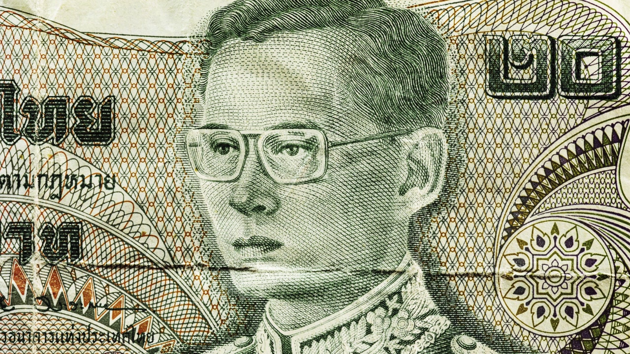 Close pan of a worn Thai baht note showing portrait, Thai text and deep fold lines