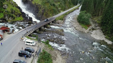 aerial forward dolly and pan showcasing tourists among låtefoss bridge at låtefossen waterfall