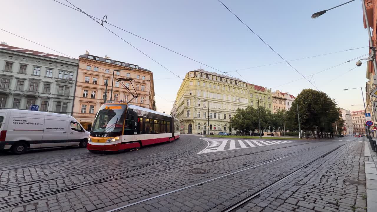 Red and white tram passes historic Prague buildings on cobblestone street in soft morning light