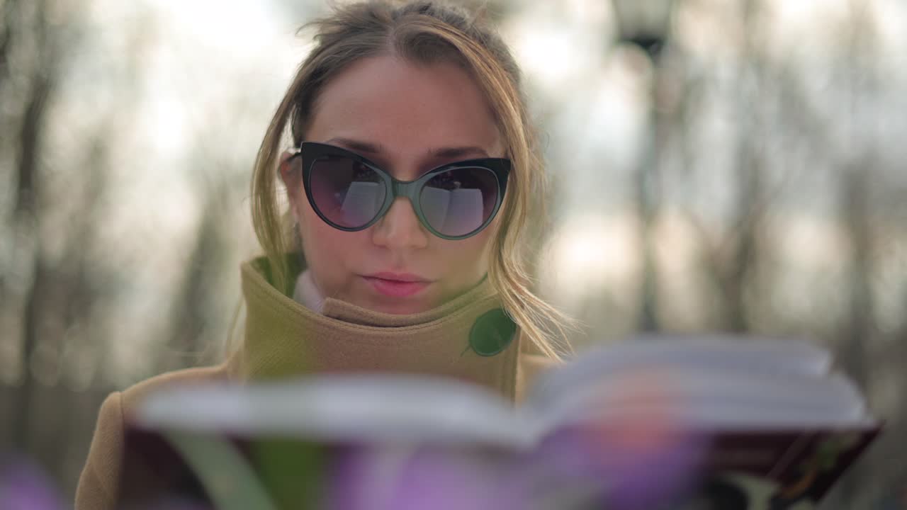 Brunette woman in brown coat reading a book at a terrace