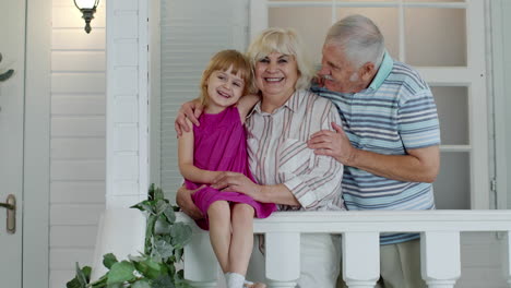 Älterer-Großvater-Und-Kleines-Mädchen-Umarmen-Großmutter-Und-Geben-Sich-Auf-Der-Veranda-Zu-Hause-Einen-Kuss