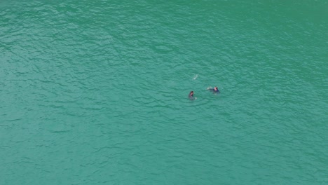 people swimming on turquoise greeny blue waters of abereiddi's blue lagoon in pembrokeshire, wales united kingdom. aerial shot