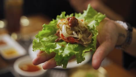 Hand-With-Ssam---Korean-Pork-Belly-Wrapped-In-Lettuce-Leaf-With-Ssamjang-And-Onions