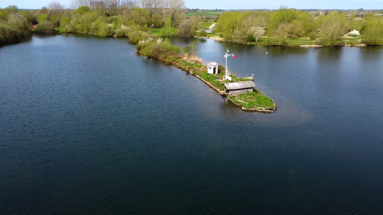 un pequeño y muy hermoso pedazo de tierra rodeado por el agua del río con un refugio construido en él, campos y árboles verdes en el fondo