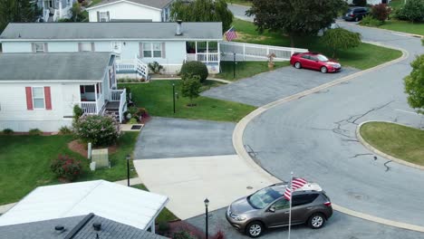 american mobile home park, usa flags flying by trailer park with cars parked in driveway, summer daytime aerial establishing shot