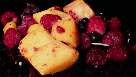 Slow-zoom-in-timelapse-of-frozen-colorful-fruits-lying-on-black-surface-in-studio,close-up