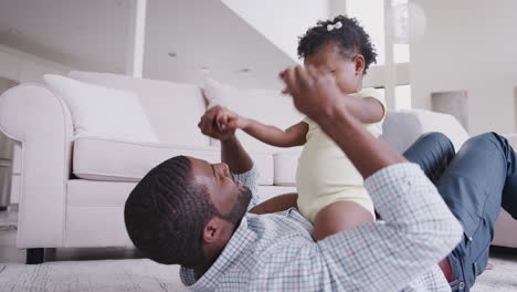 baby daughter sitting on fathers stomach as they play game at home together