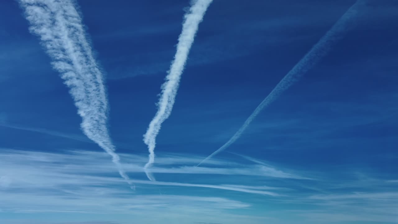 An aerial view of white parallel contrails in deep blue sky, flying at high level. Footage taken from a jet cockpit flying bellow