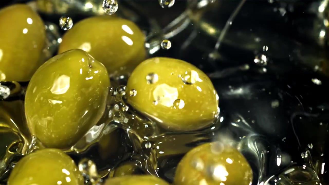 Olive verdi che cadono e schizzano nel liquido al rallentatore